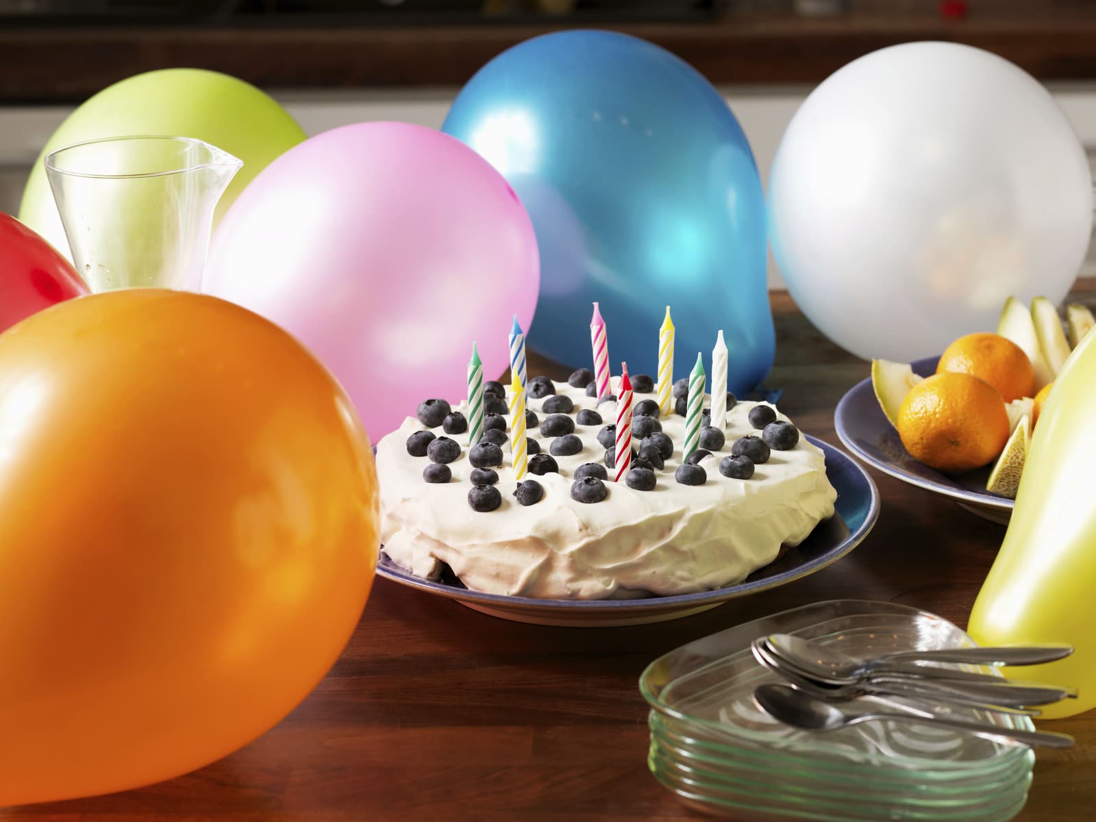 Birthday cake with blueberries and striped candles surrounded by balloons