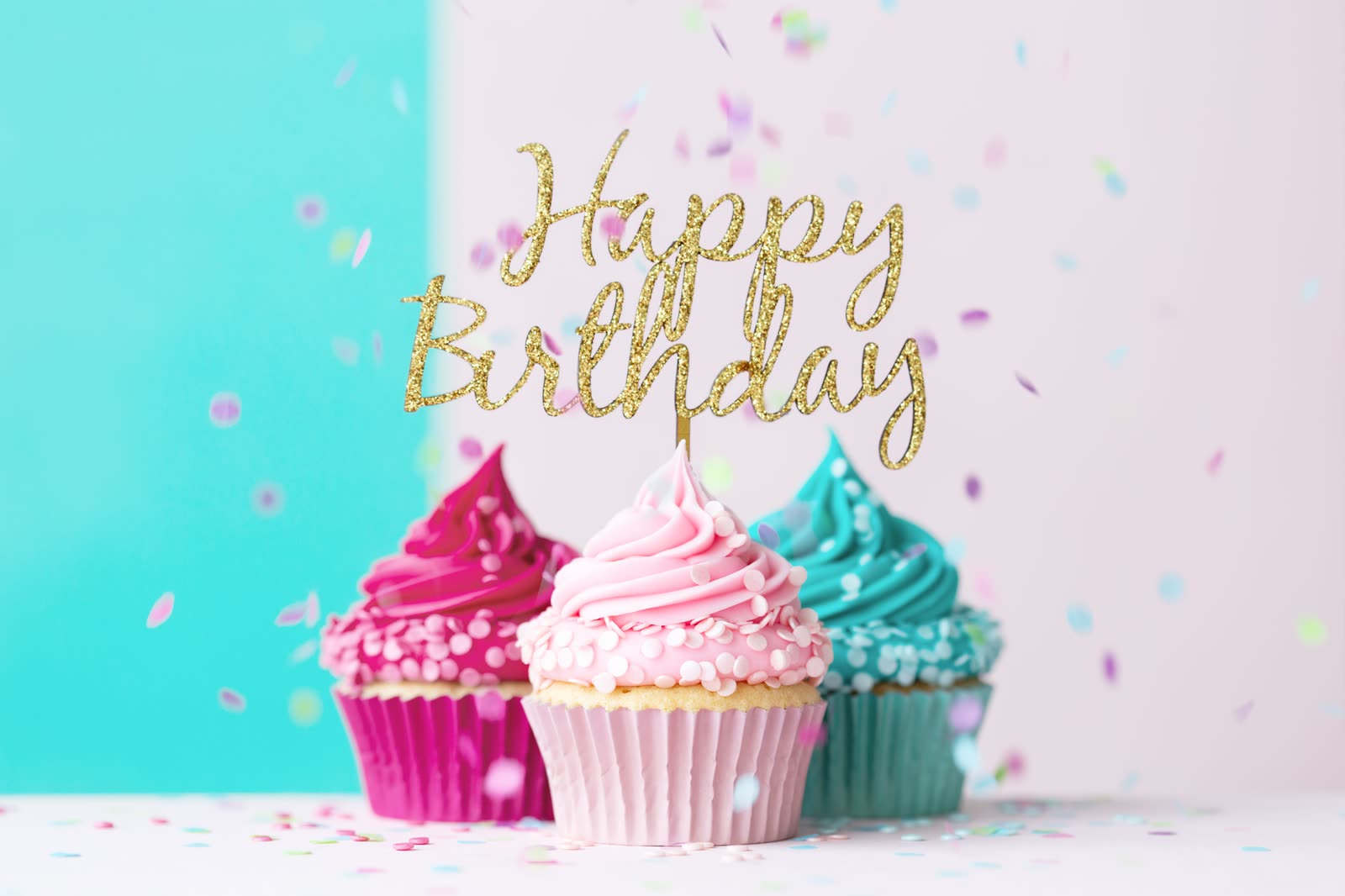 Pink and teal cupcakes with a gold Happy Birthday topper and falling confetti